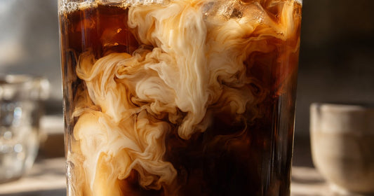 A backlit glass of iced coffee showing pale protein swirling into dark coffee